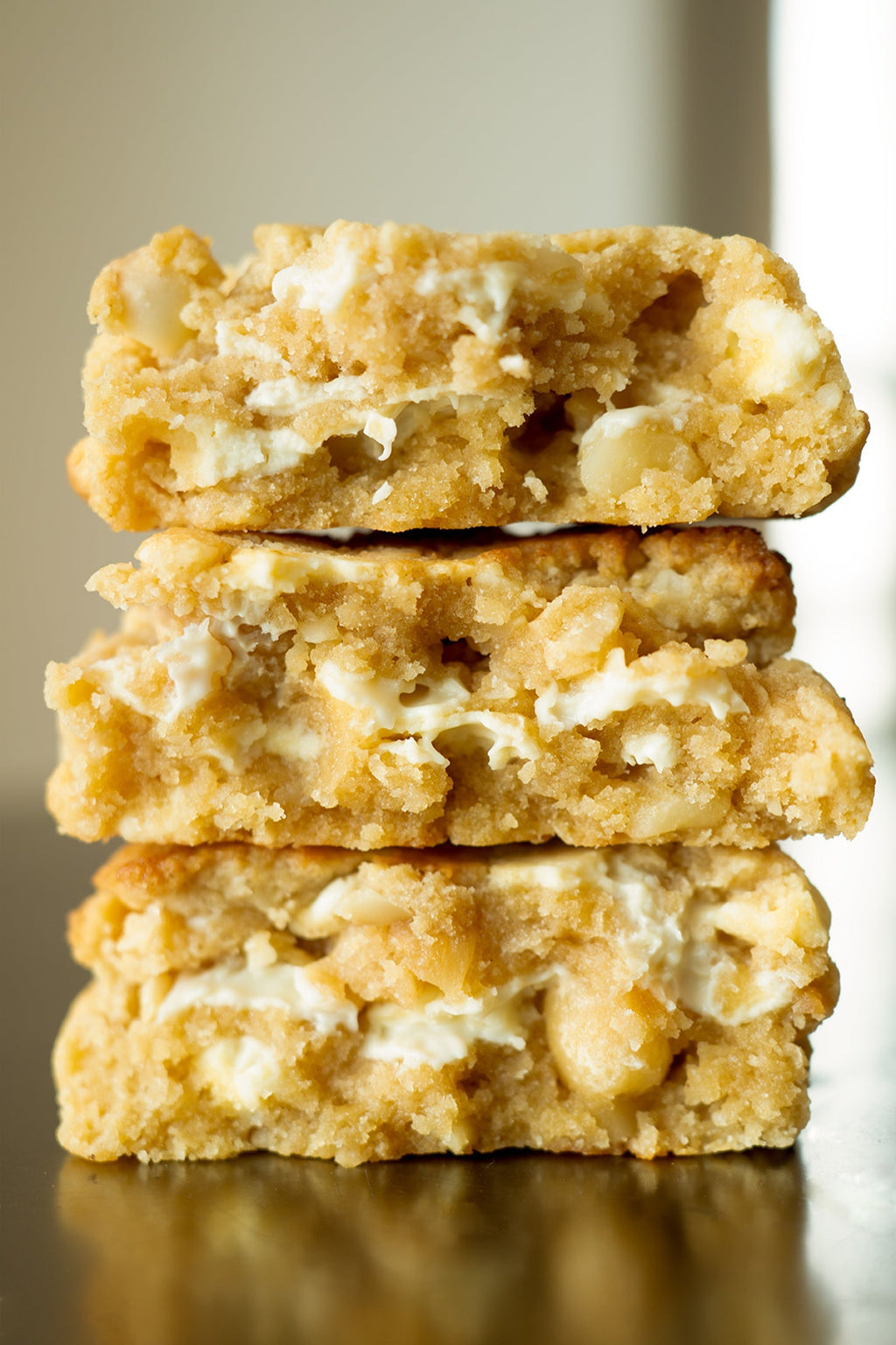 Stack of three white chocolate macadamia nut cookies on a reflective surface with a neutral background